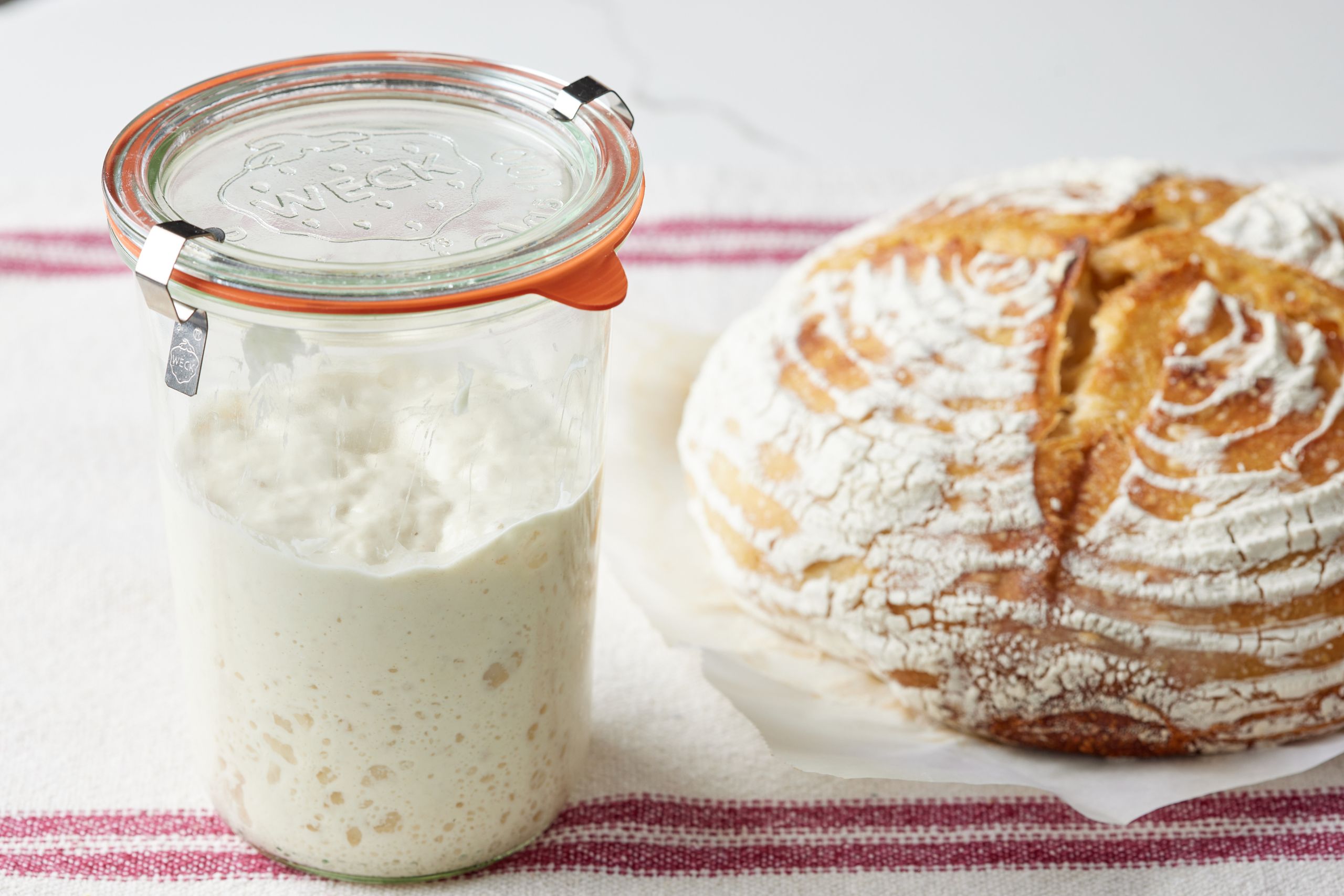 A jar of bubbling sourdough starter beside a round sourdough boule