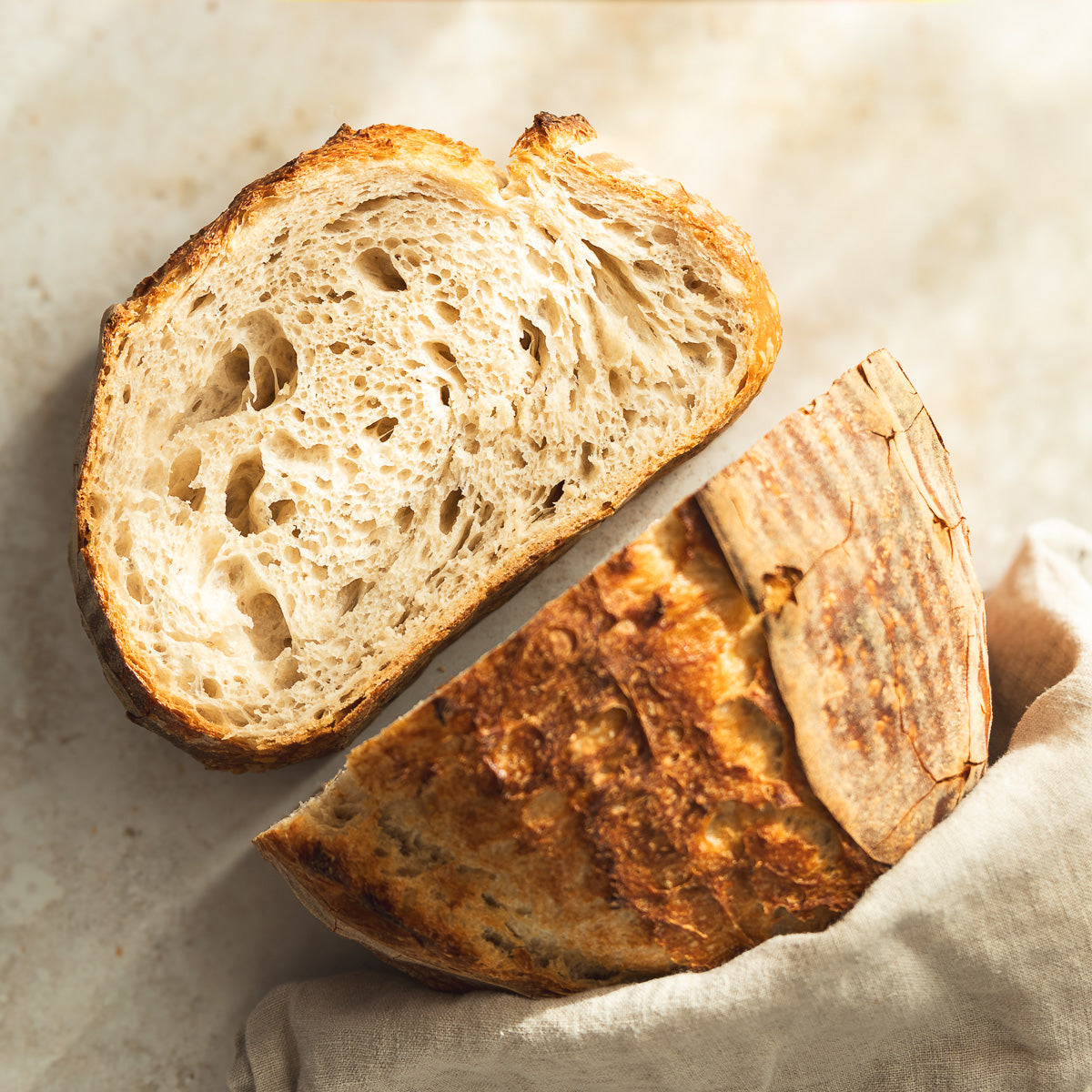 Two halves of a sliced sourdough loaf showing an open crumb, on a linen cloth